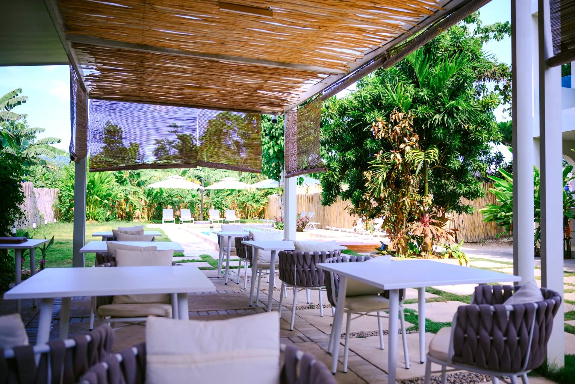 Shaded restaurant seating beside the pool and gardens