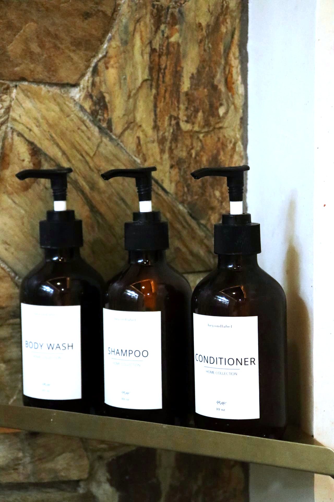 Amber amenity bottles on a brass shelf against stone
