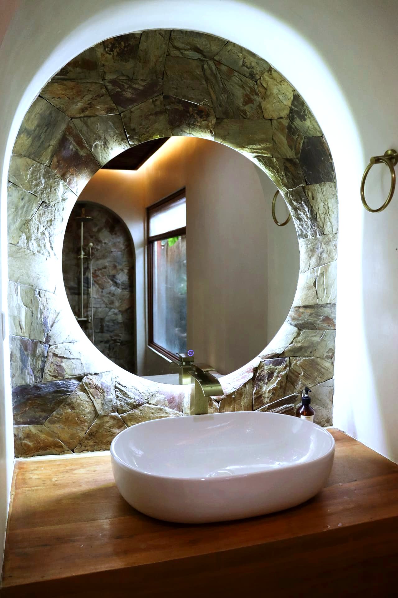 Round backlit mirror over a live-edge vanity in a stone alcove
