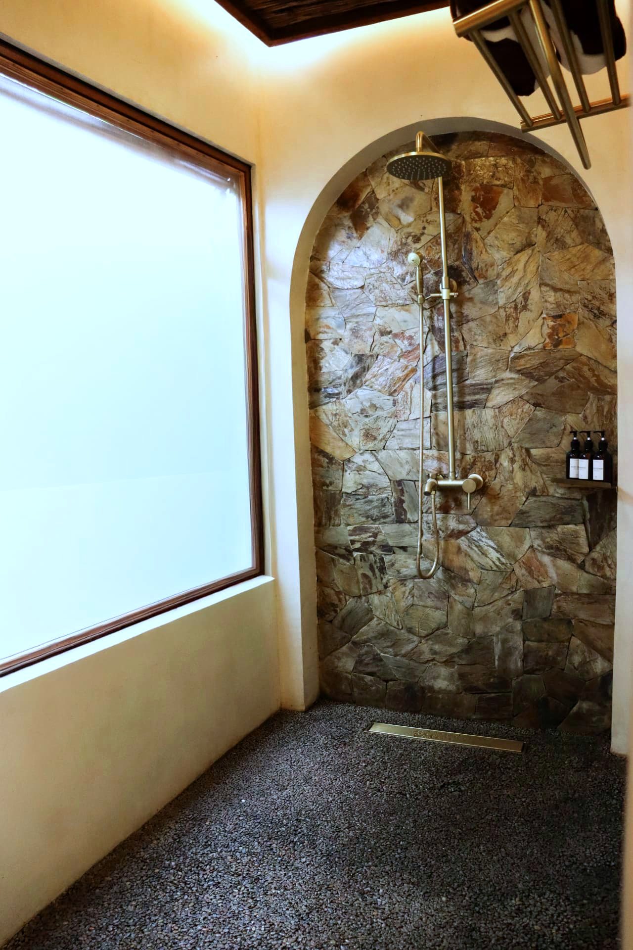 Bathroom with pebble floor and arched stone shower alcove