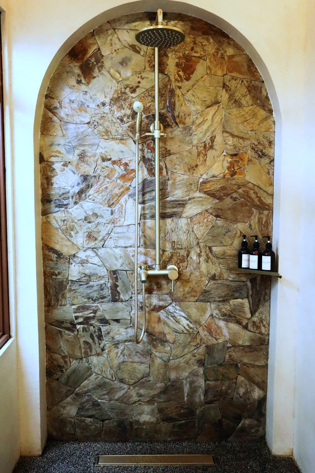 Arched stone shower with brass rainfall fixtures