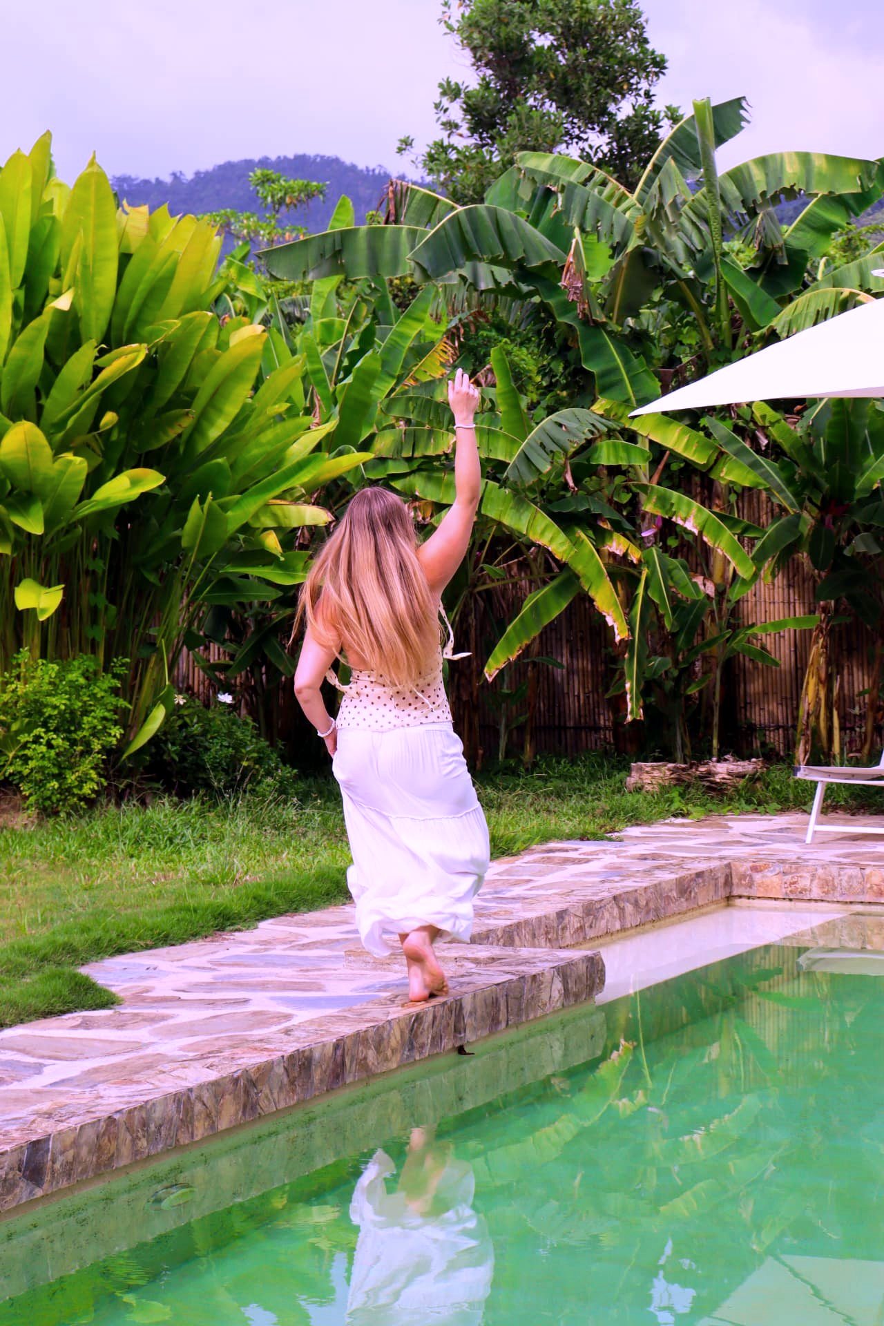 Guest walking along the pool edge framed by banana palms
