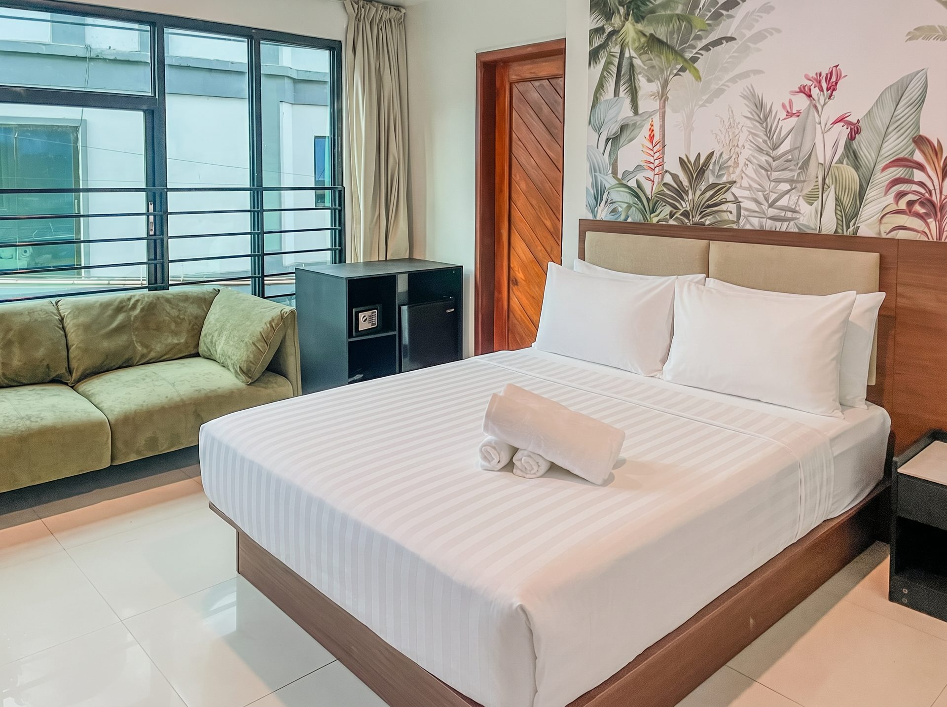 King room with green velvet sofa and tropical mural